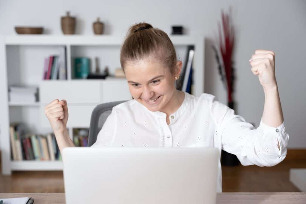 Young female student celebrating in front of her laptop