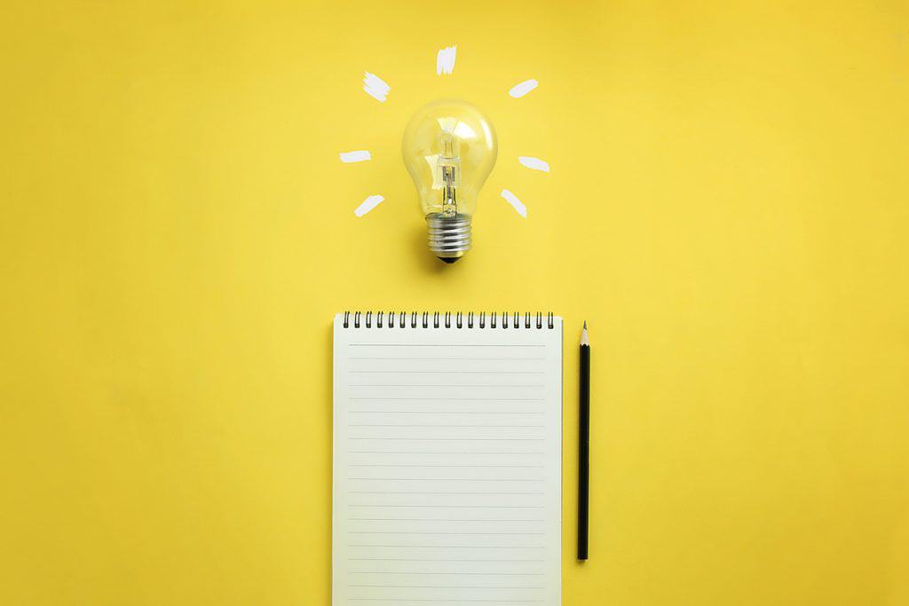 Image of a light bulb and empty memo pad and pencil on yellow background
